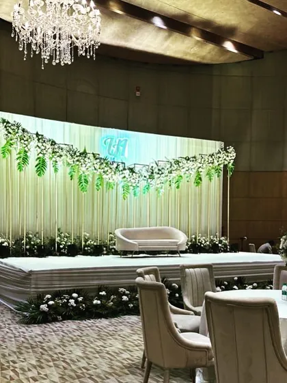 A chic and modern stage for a Roka ceremony at Andaz Delhi. The design uses clean lines, a backdrop of white strings, and a cascade of fresh greenery and white florals for a sophisticated look.