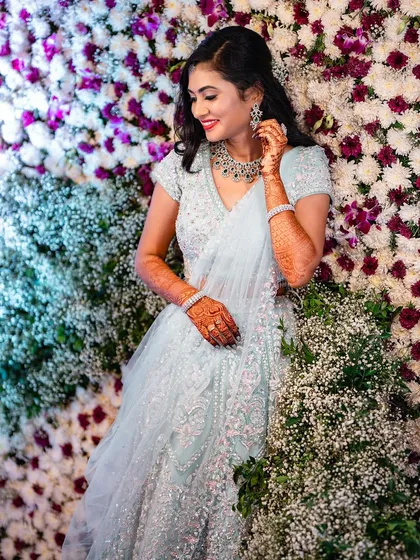 For a modern reception or sangeet, we can create something truly magical. I loved styling this shimmering lehenga with soft, romantic curls and a makeup look that felt glamorous yet effortless against this beautiful flower wall.