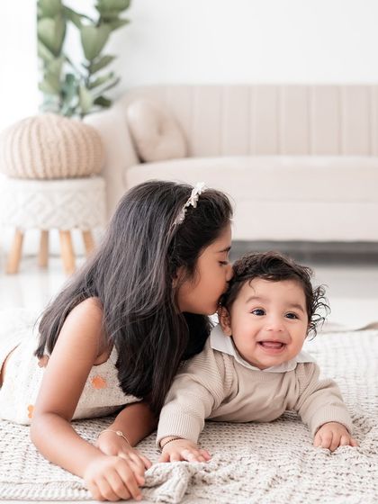 A sweet moment between two sisters. The older sister gives her smiling baby brother a kiss on the head.