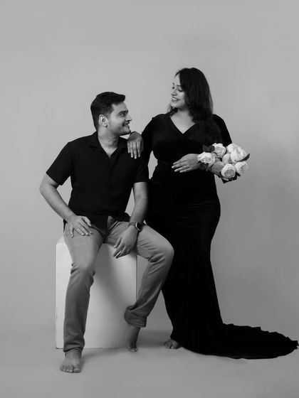 A classic couple's pose in our studio. The mother-to-be holds a bouquet of white roses, adding a touch of elegance to this black and white maternity portrait.