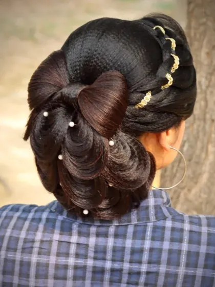 A peacock feathers bun hairstyle with a hair bow. This creative updo uses crimped hair to create a feathery texture and is adorned with pearls and a lace braid for extra detail.