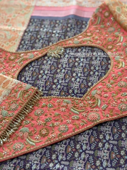 A peach-colored blouse with a keyhole back cutout. The blouse is covered in delicate floral embroidery, with a small pendant detail at the top of the cutout.