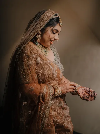 A candid moment of the bride, Laxmi, adjusting her bangles. The soft lighting beautifully illuminates her ornate lehenga and gentle smile.