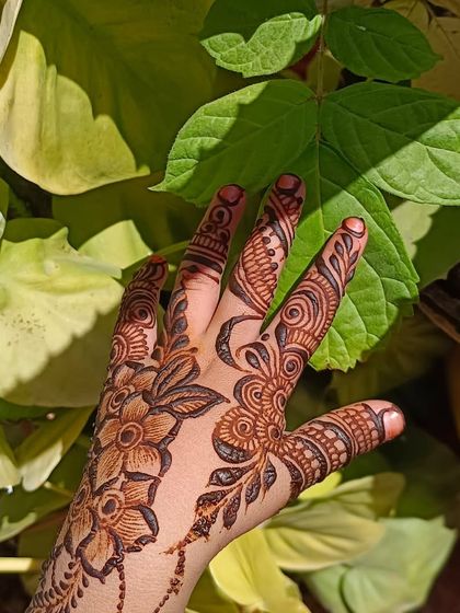 The final henna stain against a background of green leaves. This picture really highlights the rich, natural color of the floral design after the paste has been removed.