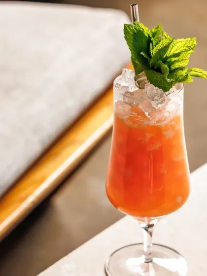 A vibrant orange-hued drink served in a hurricane glass with fresh mint. This is one of our many refreshing creations perfect for beating the heat.