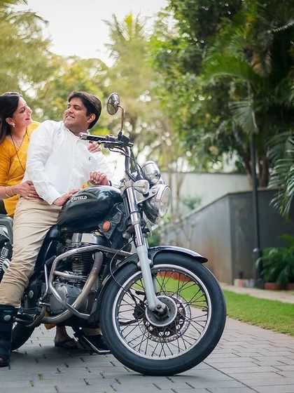 A stylish couple poses with a motorcycle during their outdoor anniversary shoot, showing off their fun and adventurous side.