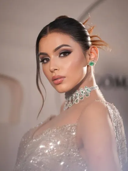 A stunning close-up portrait. The styling focuses on the smoky eye makeup and the beautiful emerald jewelry that complements the champagne gown.