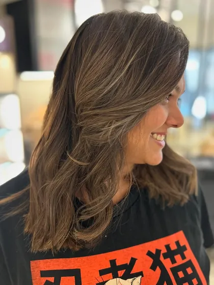 The client's happy smile shows how much she loves her new hair. The face-framing layers and warm highlights are a perfect match.