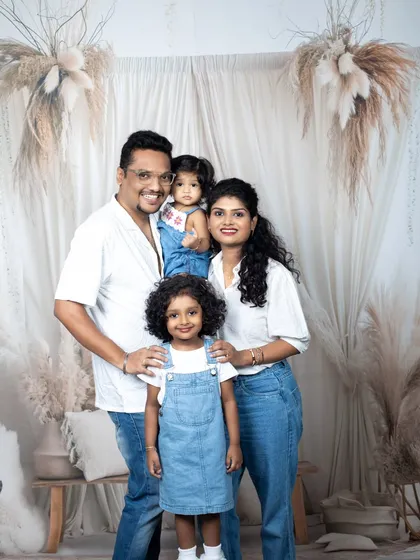 A happy family of four, dressed in coordinated white shirts and denim, sharing a genuine, joyful moment in the studio.