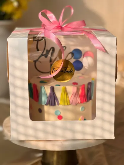 A festive and colorful cake for a first birthday party. This lemon-flavored cake is decorated with a fun tassel garland, confetti dots, and a balloon topper.