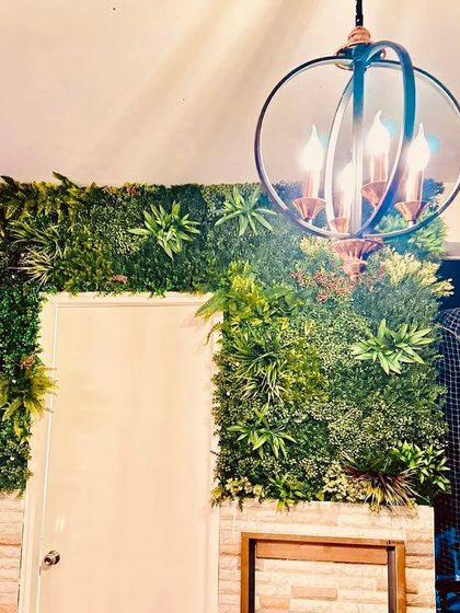 A view of the door-framing installation at night. The interior lighting, including a modern chandelier, interacts with the foliage to create a warm and sophisticated ambiance.