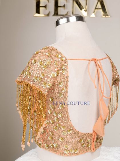 This peach-toned blouse is all about the sparkle and movement. It's crafted from net and covered in sequin and zardozi floral motifs, with dramatic, dangling beaded tassels on the sleeves for a show-stopping effect.
