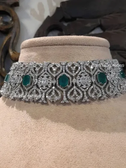 A close-up of a stunning diamond and emerald choker. The design features a beautiful pattern of pavé-set diamonds interspersed with rich, oval-cut emeralds, creating a piece that is both classic and luxurious.