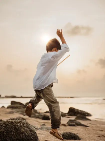 A boy leaps across rocks on the beach at sunset. This action shot captures the adventurous and energetic spirit of a child.