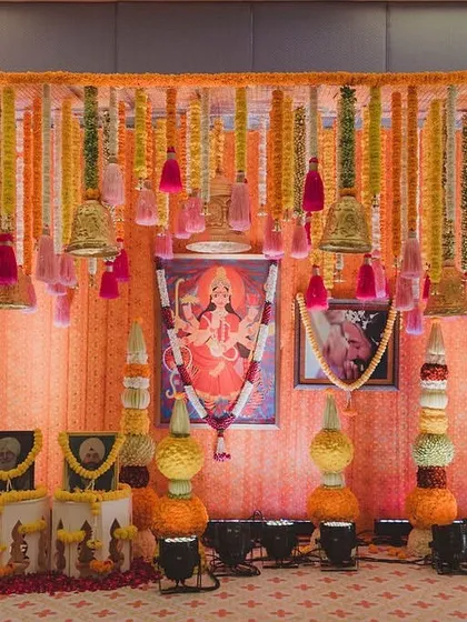 The main stage for Ayesha and Madhav's Mata ki Chowki. The decor is rich with traditional elements like hanging bells, marigold garlands, and a central portrait of the deity, creating a deeply spiritual and festive space.