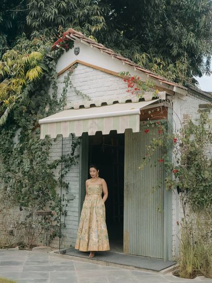 A beautiful portrait of Nikita at her Haldi ceremony, standing in a rustic doorway covered in vines. This image captures a moment of quiet grace amidst the colorful festivities.