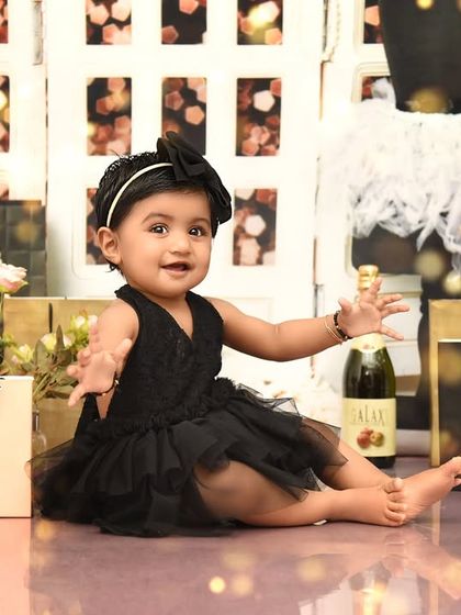 Reaching out to welcome her guests to her stylish first birthday shoot. The setup includes a vanity mirror, pearls, and shopping bags for a complete fashion experience.