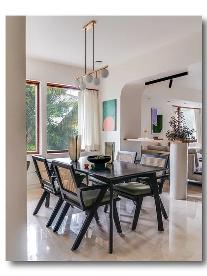 A sophisticated dining area featuring a dark wood table and chairs with caned backs. The large windows let in ample light, while the modern globe chandelier adds a touch of contemporary elegance.