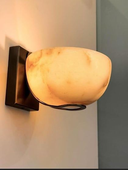 A bowl-shaped wall sconce made of alabaster. The natural veining of the stone is illuminated from within, creating a soft and elegant ambient light.