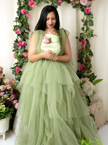 A stunning portrait of a mother in a green gown holding her swaddled baby, looking like a goddess of nature.