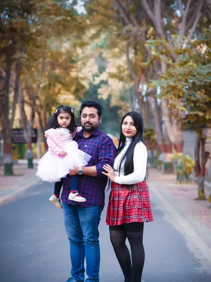A full-length family portrait taken on a tree-lined road, showcasing the family's coordinated outfits and happy smiles.