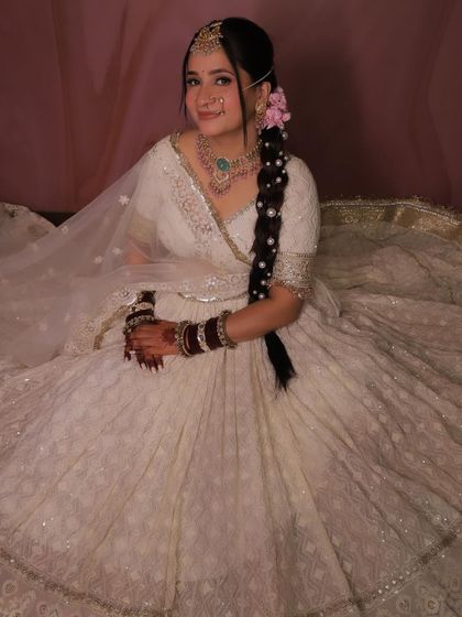 An elegant pose in our white designer lehenga. The pearl-adorned braid complements the outfit's intricate work.