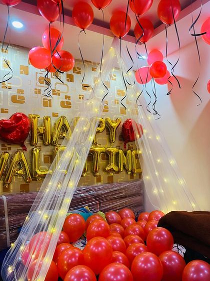 A vibrant Valentine's Day surprise with the room filled with red balloons and a "Happy Valentine" message in gold foil letters over the bed.