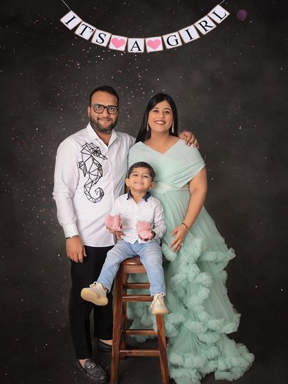 It's a girl! This sweet family portrait uses a banner and adorable pink booties to share the happy news, with the mom-to-be glowing in a mint green ruffled gown.