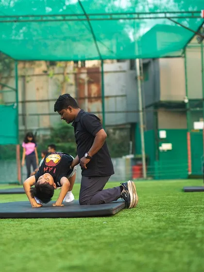 A coach helps a young boy with his backbend, ensuring his form is correct and his muscles are developing properly.