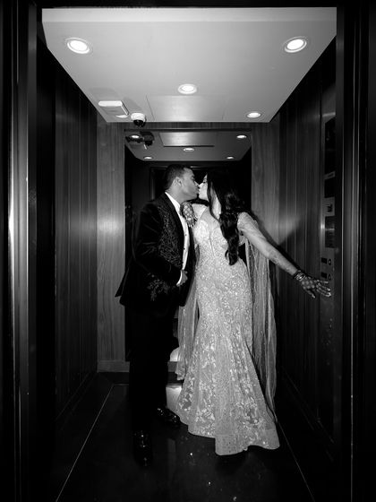 A playful and intimate black and white shot of Aabhaas and Radhika sharing a kiss in an elevator. This candid moment captures their fun-loving spirit during their engagement night.