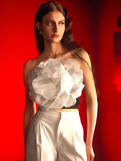 A powerful and bold composition. The stark contrast between the vibrant red background, the crisp white pants, and the sculptural white top creates a visually arresting and modern fashion statement.