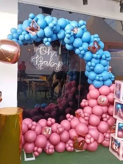 An 'Oh Baby' gender reveal setup with a pink and blue balloon arch, a gold plinth, and 'BABY' boxes.
