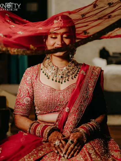 A beautiful, candid moment of the bride as her veil playfully covers her face. This shot captures her natural smile and the delicate movement of her red dupatta, creating a soft and romantic bridal portrait.