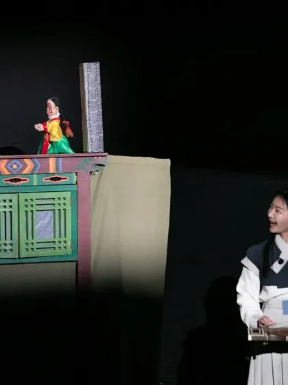The musician for 'Hong Dongji & Isimi' smiles as she watches the puppets interact on stage. The synergy between music and puppetry is key to the show's success.