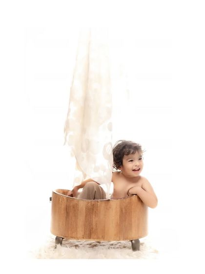 Pure joy in the tub. A toddler laughs happily while sitting in a wooden bathtub prop during a fun studio session. This playful and candid shot is all about capturing genuine, uninhibited happiness.
