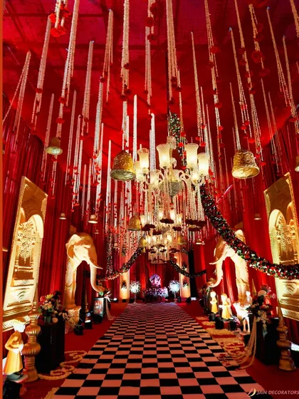 A royal entrance for a traditional wedding. The pathway is lined with statues of elephants and a checkered floor, leading into a space draped in opulent red and gold.