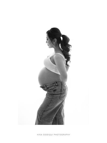 A wider view of a classic solo maternity portrait. The clean white space and monochrome tones make this a perfect example of minimalist fine art photography.