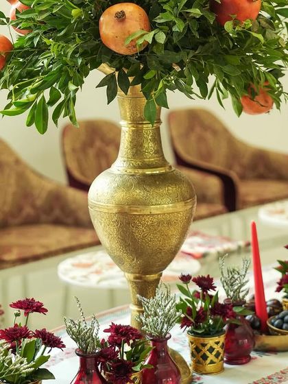 A detail shot of the tablescape, with a tall brass vase holding a pomegranate branch, and smaller red vases with flowers, creating layers of visual interest.