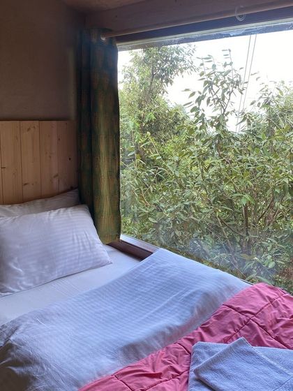 A simple, clean, and comfortable bed in one of our rooms, with a window that opens up to nature. A perfect space to rest and dream up new worlds.