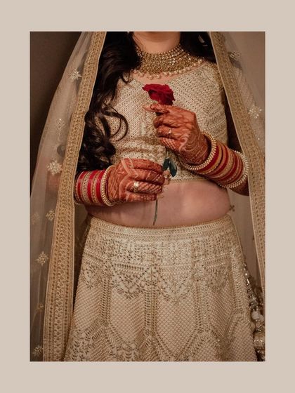 An elegant portrait of a bride in a white lehenga holding a single red rose. The contrast of colors and her graceful pose make this a timeless and romantic shot.