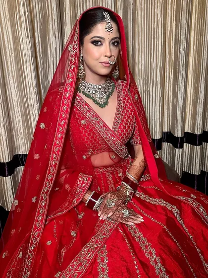 A traditional Indian bridal look featuring kohl-lined eyes and a dewy skin finish. This makeup is designed to complement the classic red Sabyasachi lehenga, creating a look that is both timeless and beautiful.
