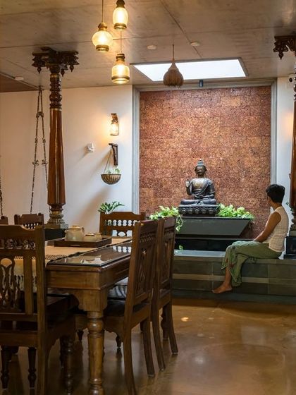 A serene seating area next to the courtyard features a Buddha statue against a textured laterite wall, creating a space for quiet contemplation.