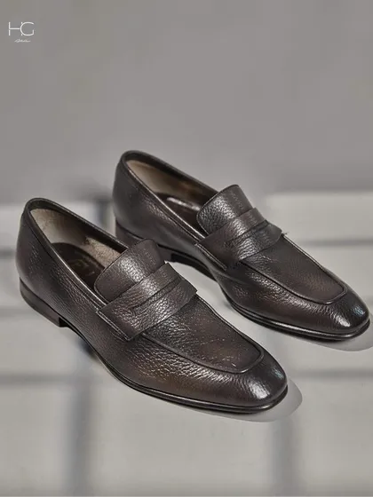 A closer look at the textured grain of these leather penny loafers. The craftsmanship is evident in the stitching and the rich patina of the leather.