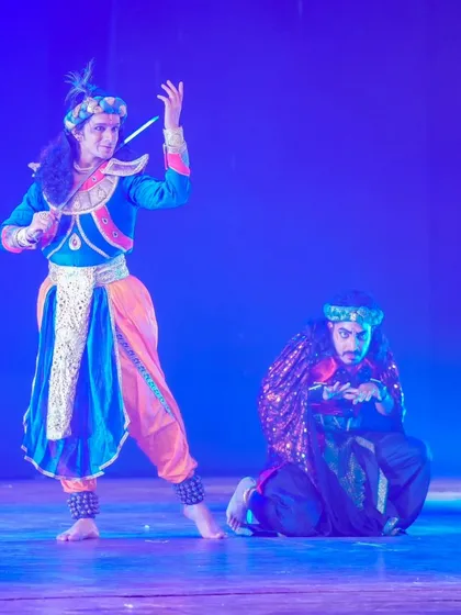 Krishna's commanding presence on stage. The costume, with its intricate headgear and armor, is designed to evoke a sense of divinity and royalty.