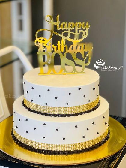 A simple and elegant cake for a boss's birthday. The two-tier design with black polka dots and gold ribbon is professional yet celebratory.
