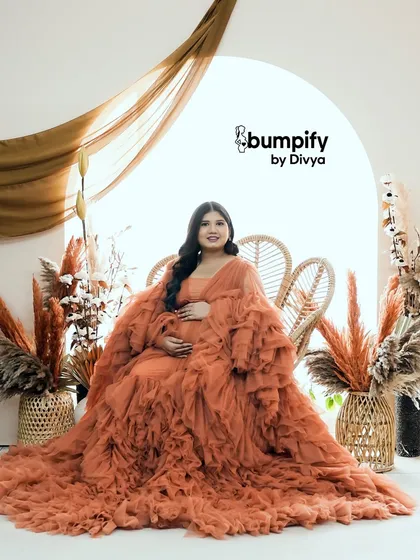 A solo portrait of the mom-to-be in the orange gown, seated on a wicker chair. This shot captures her serene beauty and the joyful anticipation of motherhood.