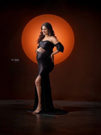 A full-length portrait in a sequined black gown, set against a warm, glowing circular backdrop that creates a beautiful halo effect.