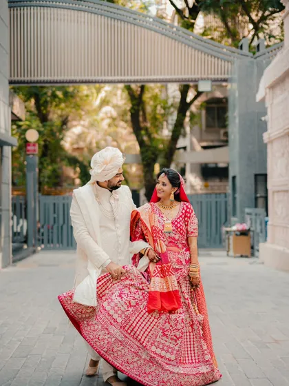 A playful and candid moment on the street. The groom lifts the bride's lehenga as they share a look, showcasing their fun loving connection.