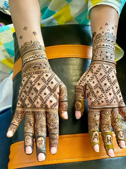 A fully personalized design with the initials 'A' and 'H' on the fingertips and 'Shri' and 'G' on the other hand. The intricate jaal (net) pattern completes this custom piece.