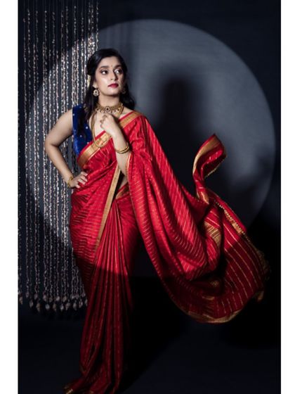 A dynamic shot of the model in a red saree, with the fabric flowing to create a sense of movement. The spotlight effect adds a touch of drama to this festive fashion shot.